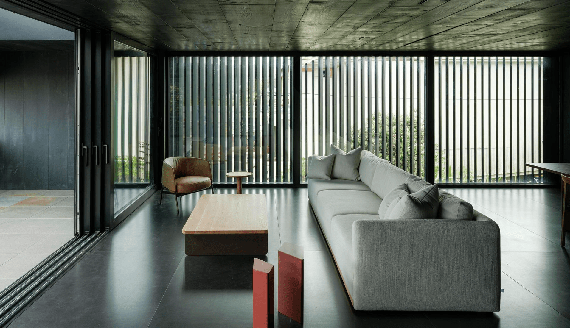 Modern living space with timber slat screens, gray sofa, and polished concrete floors