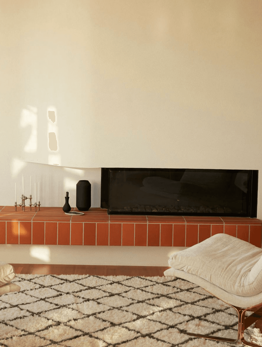 Warm living room with terracotta-tiled floating hearth, black gas fireplace, and diamond-pattern rug