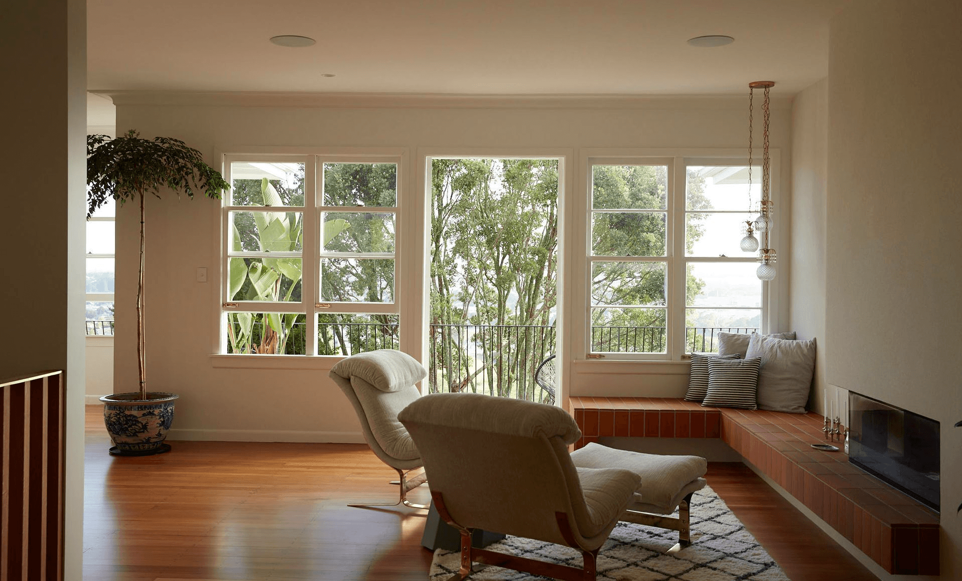Bright living room with white-framed windows, wooden floors, and a terracotta-tiled window seat bench