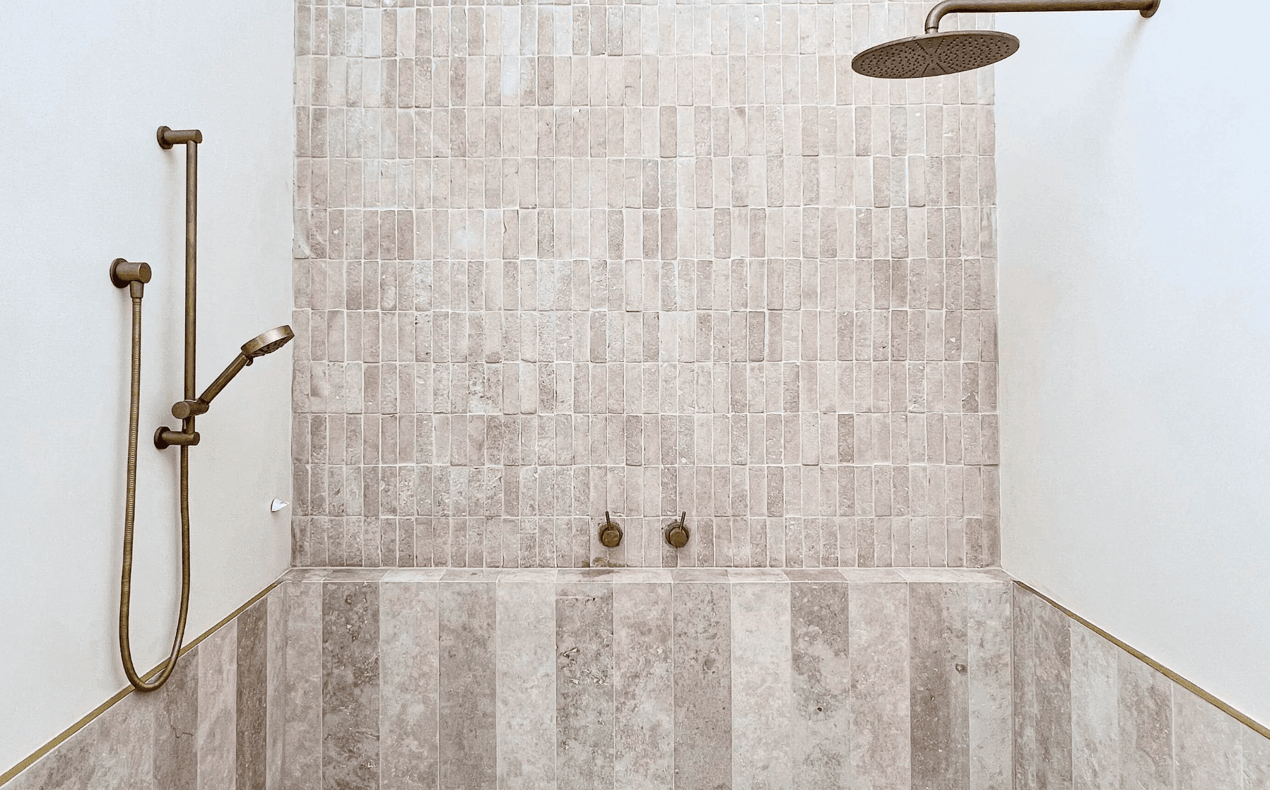 Walk-in shower with beige travertine mosaic tiles and brushed brass rainfall and handheld fixtures