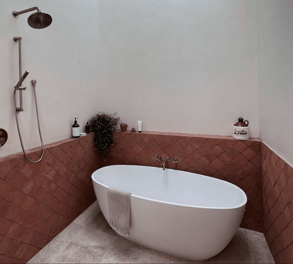 Bathroom with terracotta diamond-pattern wall tiles, white freestanding bathtub, and stone flooring
